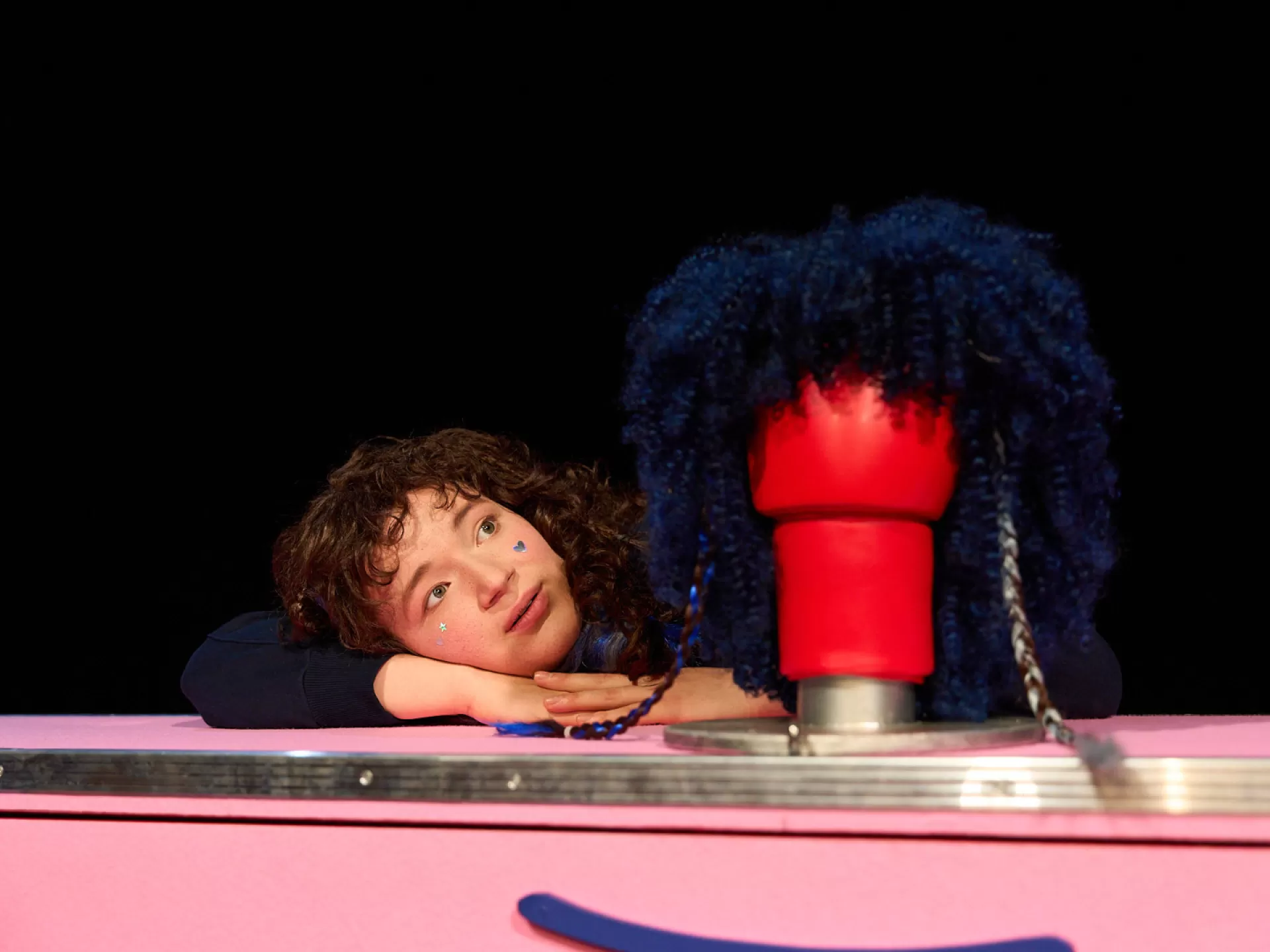 EIne Person mit Locken schaut auf einen Boxhandschuh, dem eine lockige Perücke übergeworfen ist