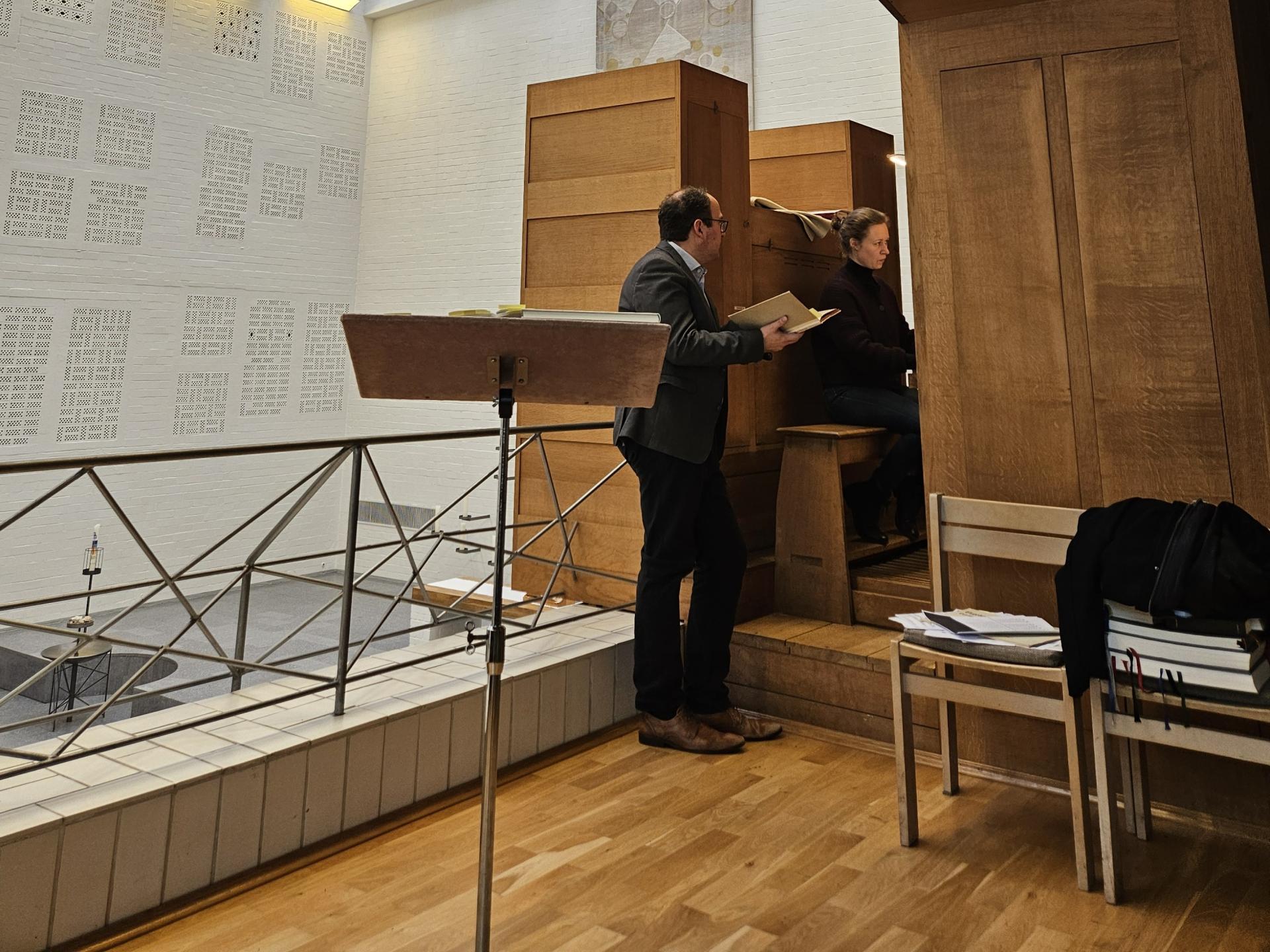 Prof. Jens Wollenschläger gab auch individuelle Hinweise zu den vorbereiteten Stücken. Jens Wollenschläger steht an Orgel, hält ein Buch, Studentin sitzt am Spieltisch und spielt