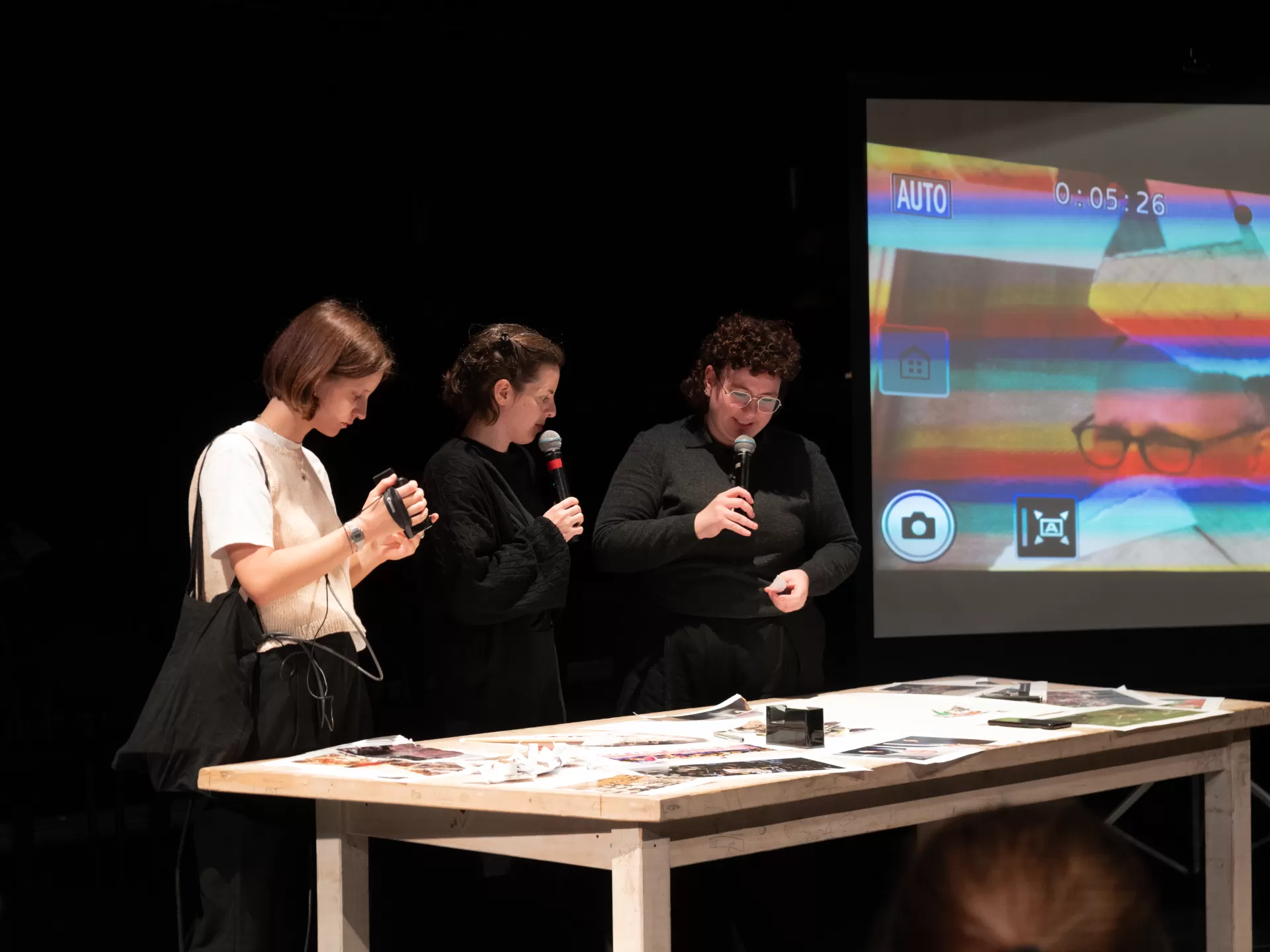 Drei Personen stehen an einem Tisch mit ausgedruckten Bildern.