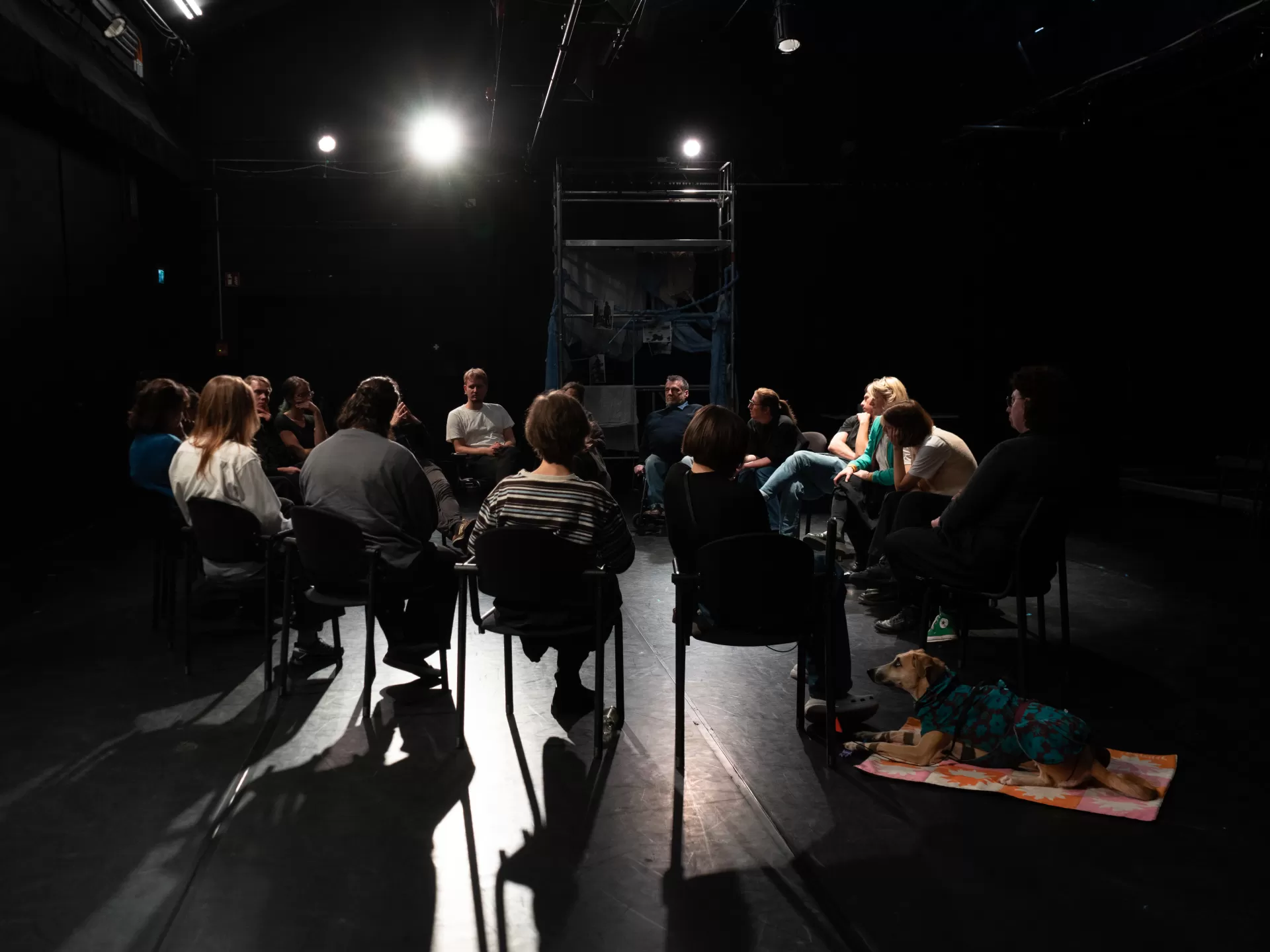 Personen sitzen in einem Stuhlkreis auf einer Bühnenfläche.