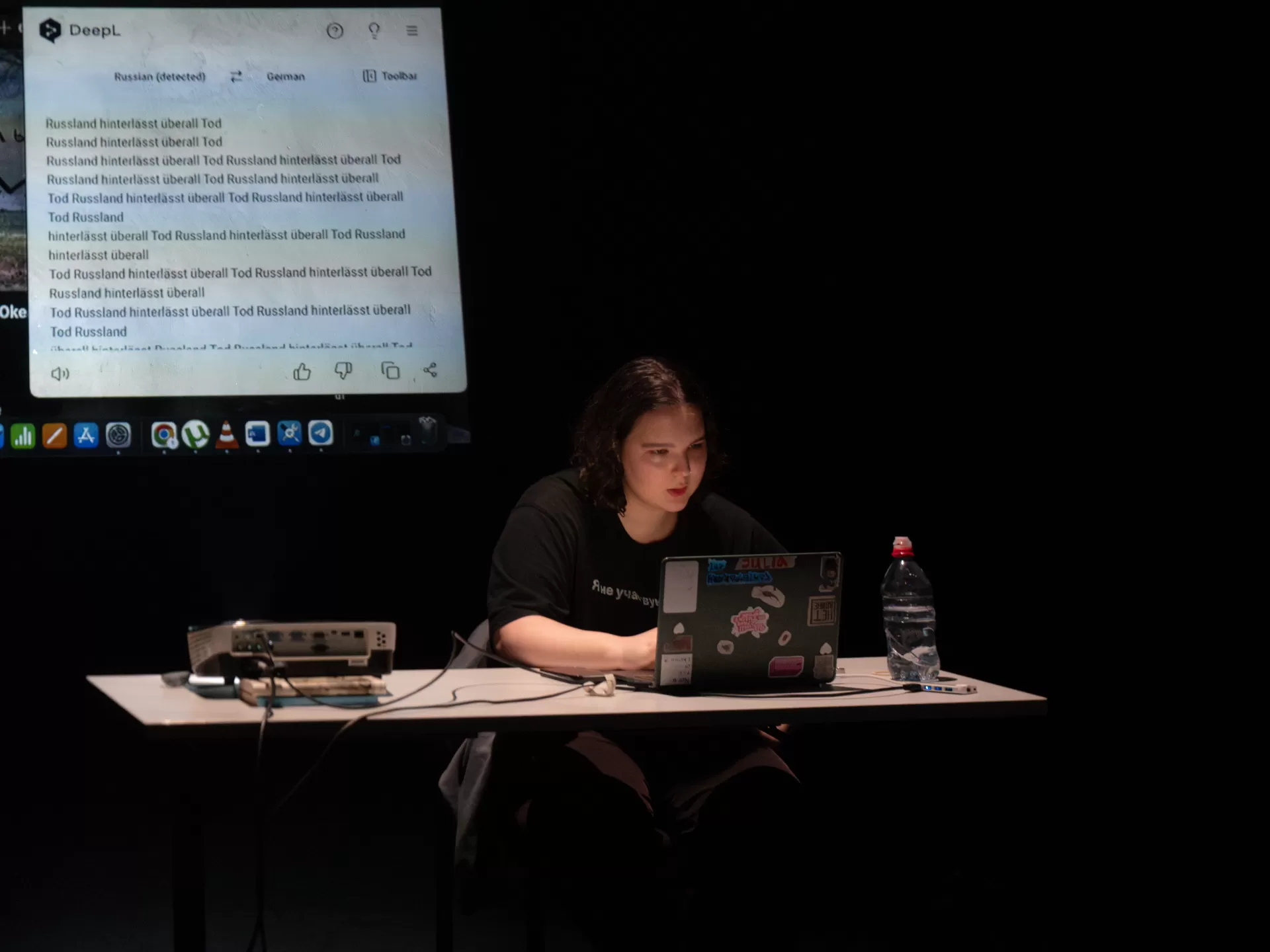 Eine Person sitzt mit Laptop an einem Schreibtisch, hinter ihr die Videoprojektion einer Google-Suche.