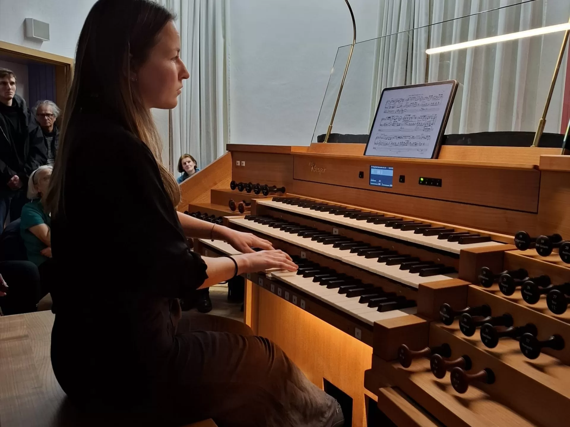 Studentin spielt an der Rieger-Orgel, im Raum sitzen viele Menschen um sie herum