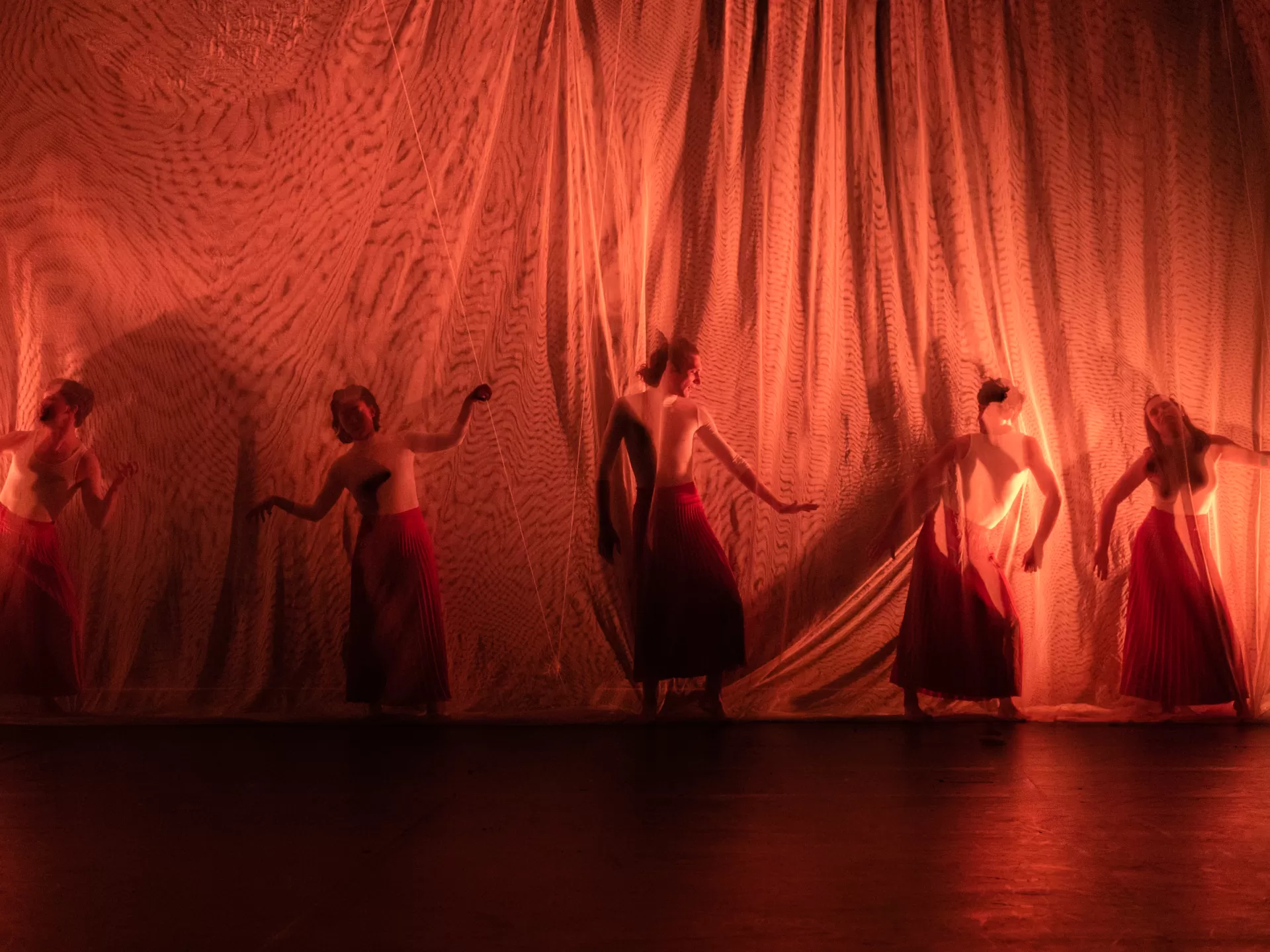 Personen in tanzenden Positionen hinter einem transparenten Vorhang.