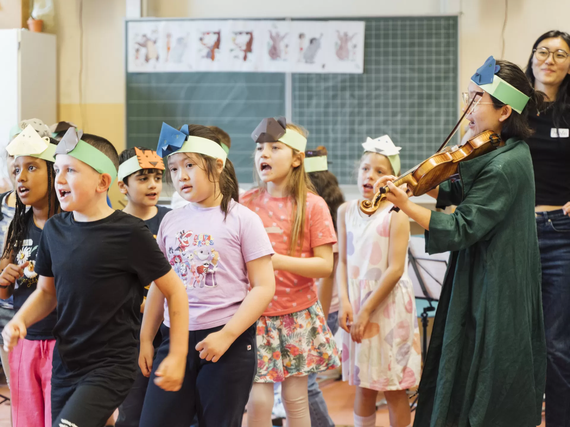 Schüler*innen bewegen sich zur Musik, die von einer Geigerin im Klassenraum gespielt wird.