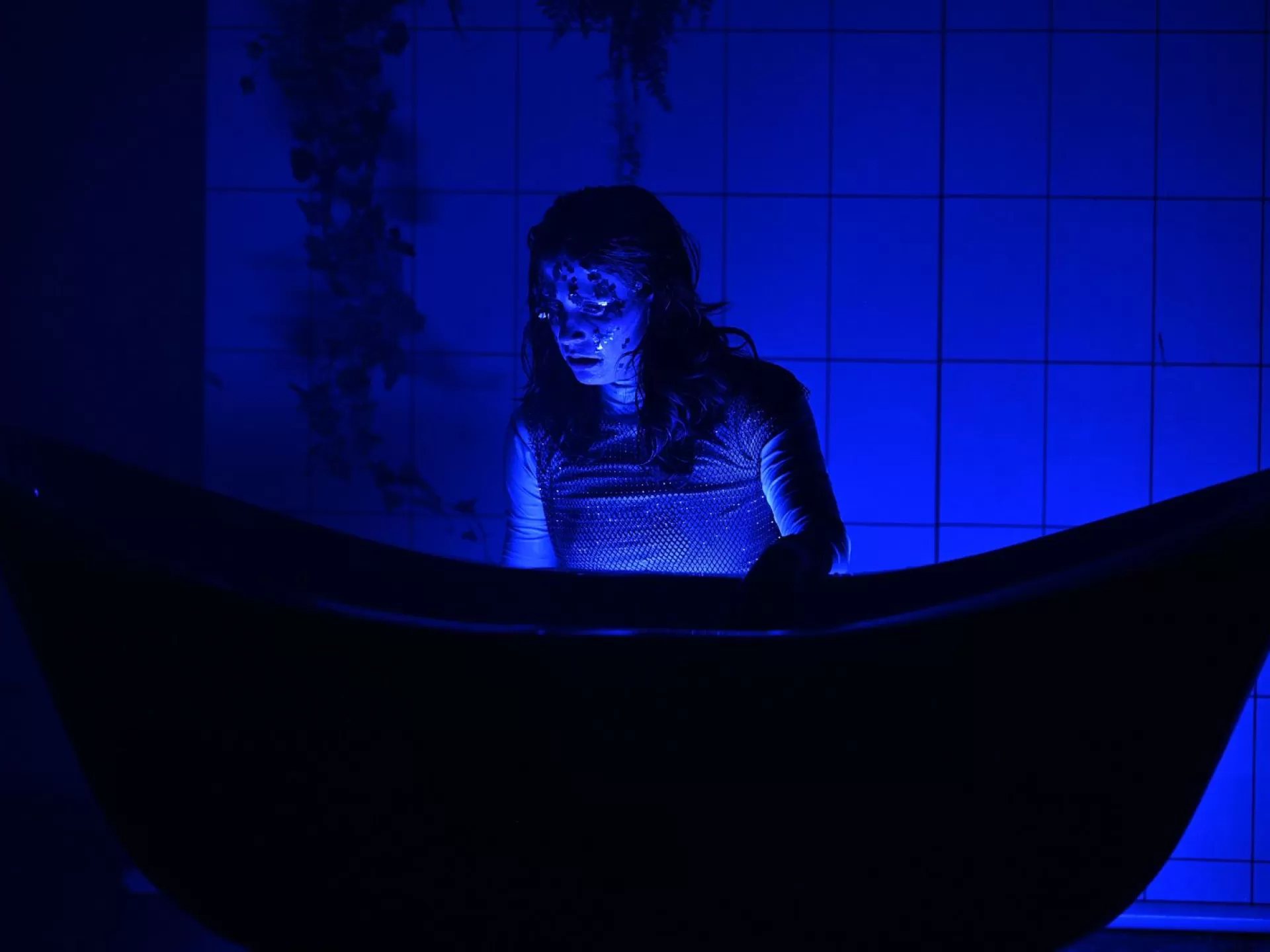 eine junge Frau kniet vor einer Badewanne. Blaues Licht um sie.