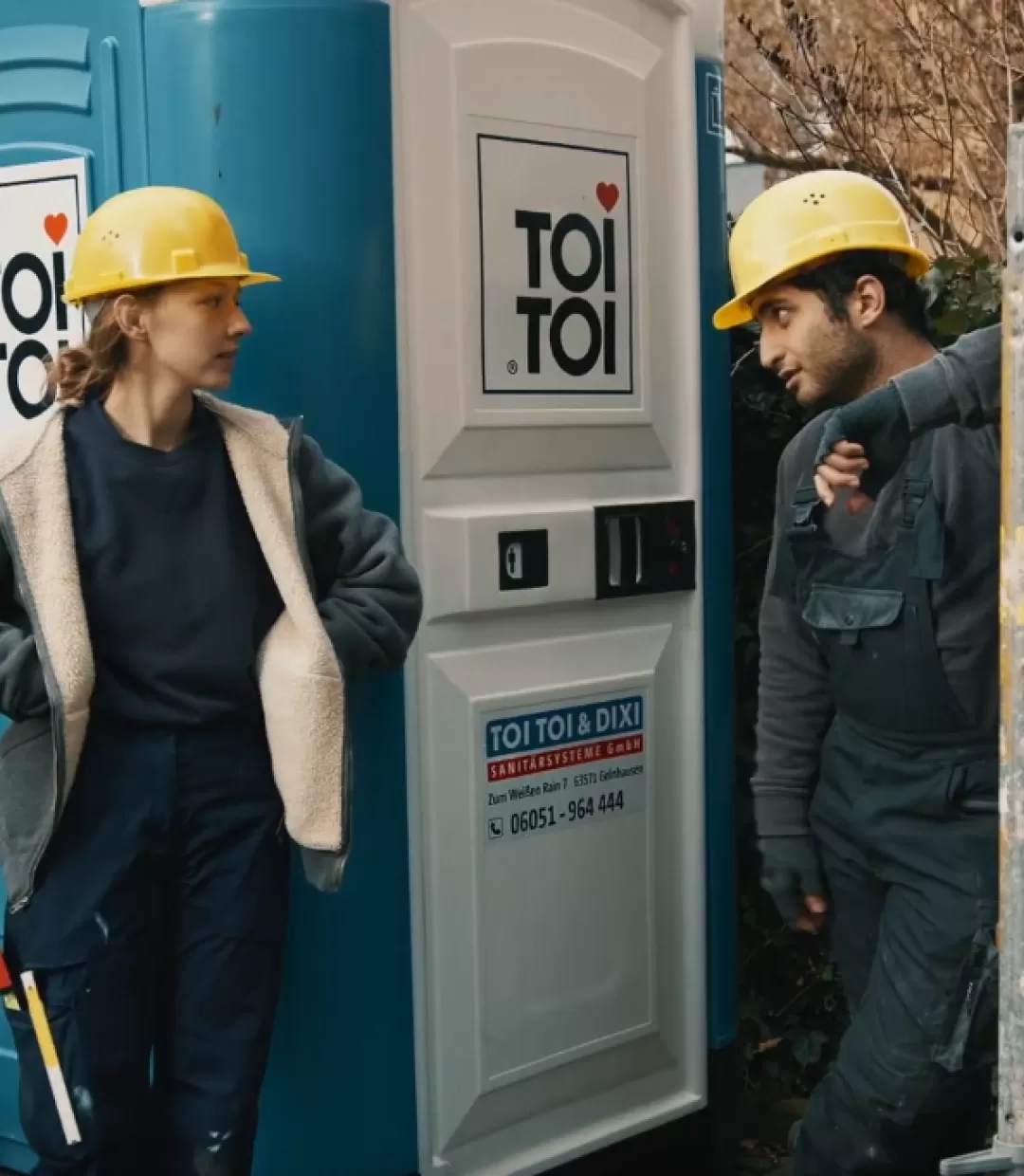 Ein Bauarbeiter und eine Bauarbeiterin stehen für einer Dixi-Toilette.