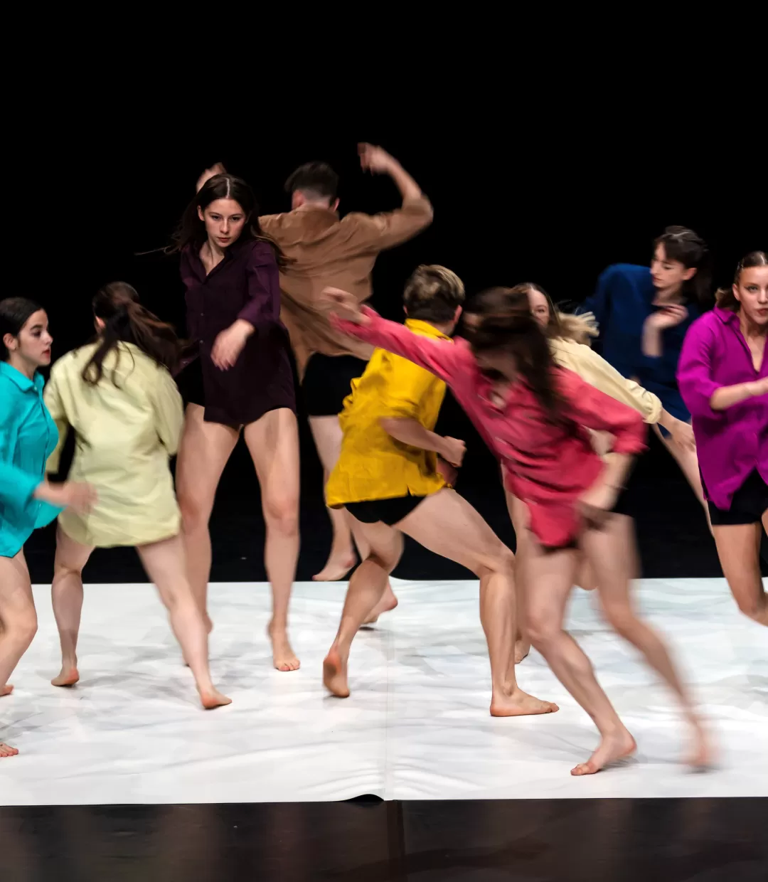 Gruppe von 8 Tänzer*innen in bunten Hemden, in dynamischer Bewegung fotografier.
