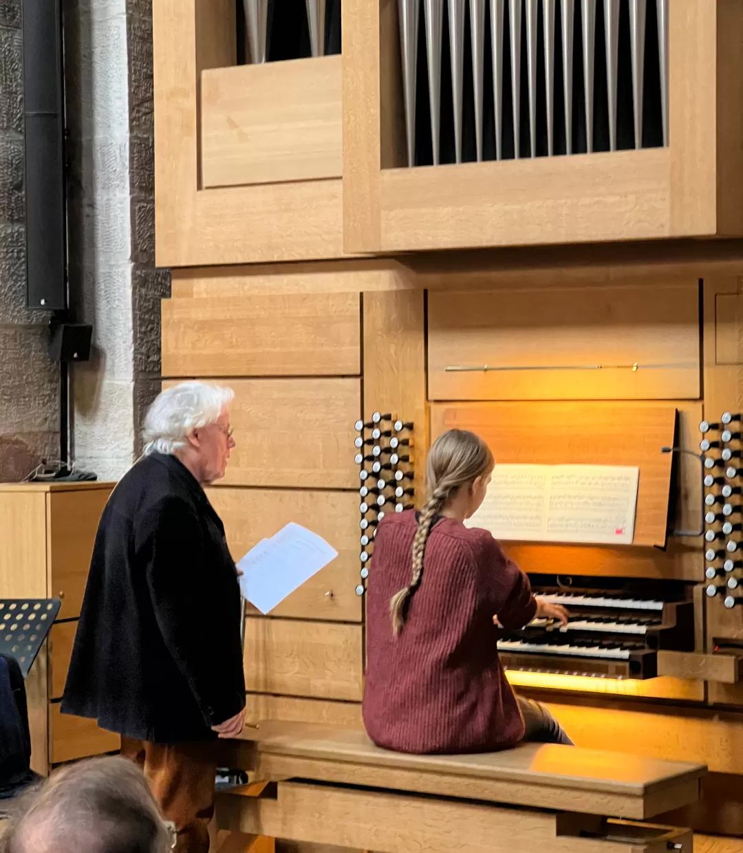 Studentin sitzt an der Orgel, Daniel Roth steht daneben und erklärt etwas