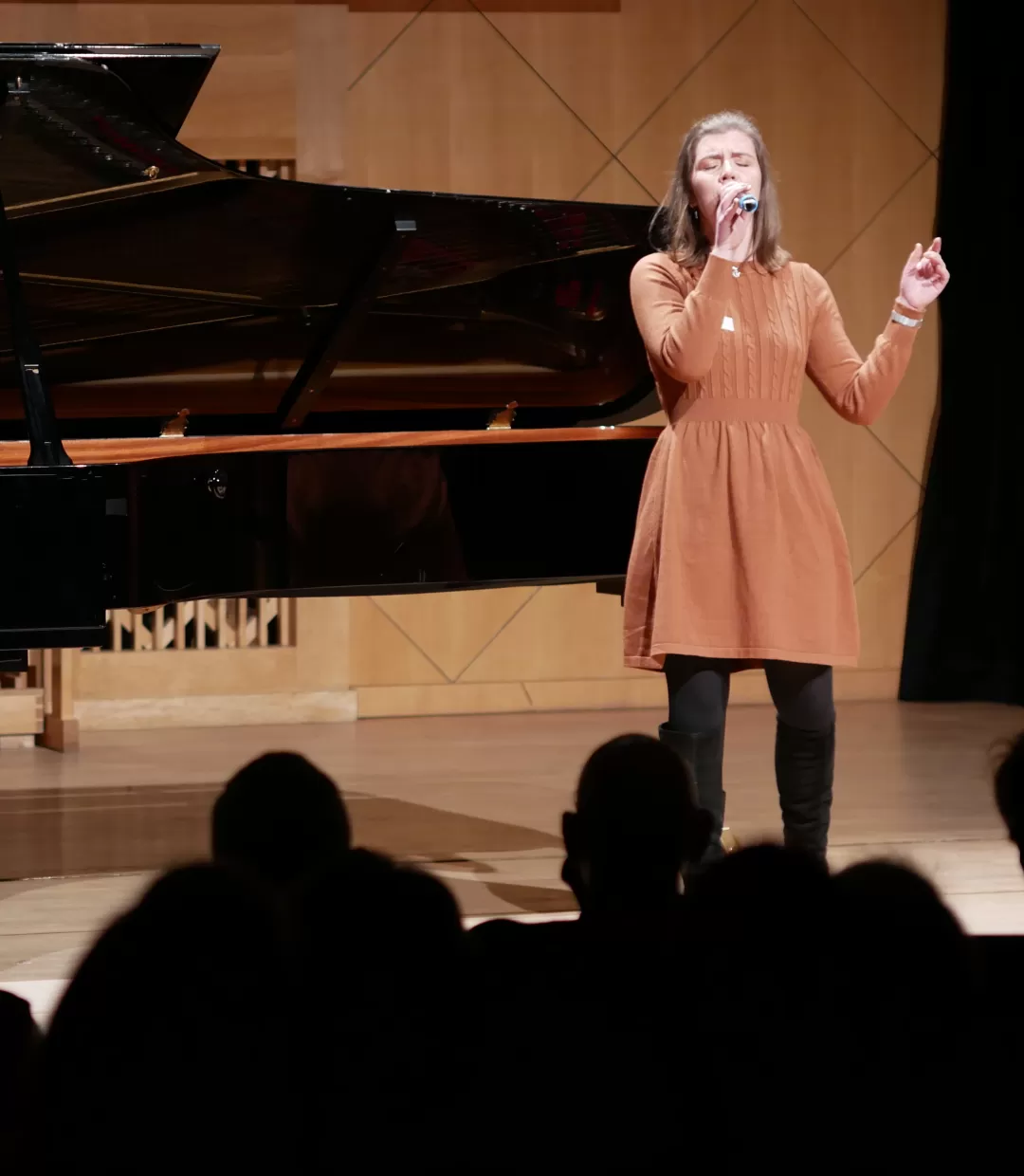 Eine vor Publikum singende Studentin mit Mikrofon. Sie wird von einer Person am Flügel begleitet.