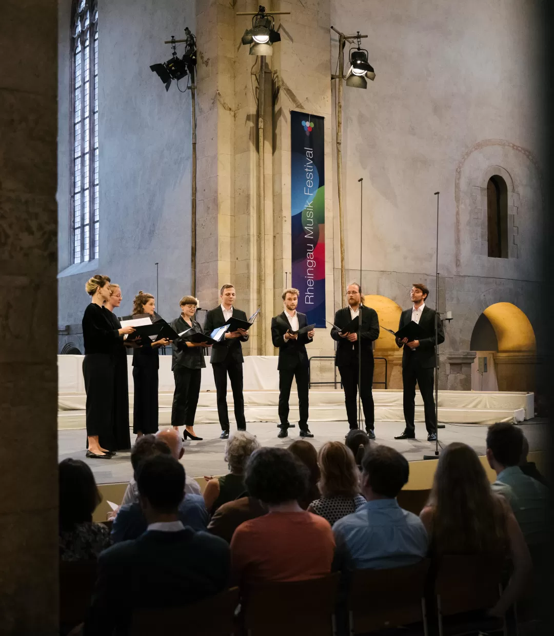Die acht Sänger*innen des Ensembles Et Hepera auf der Bühne im Kloster Eberbach. Im Vordergrund ist Publikum zu sehen.
