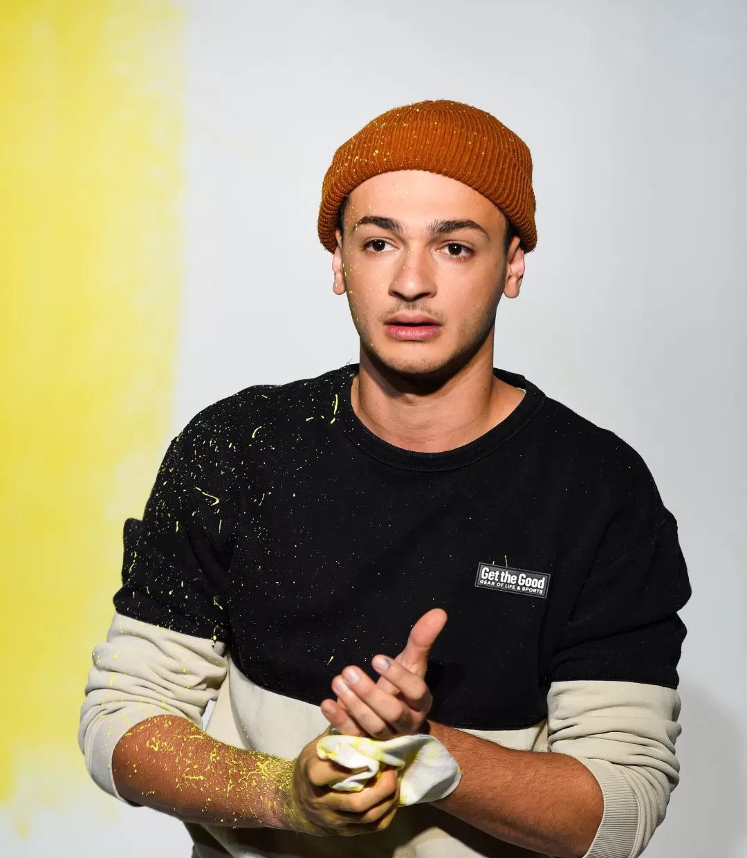 Schauspieler steht vor einer bemalten Wand und wischt sich mit einem Tuch Farbe von den Händen.