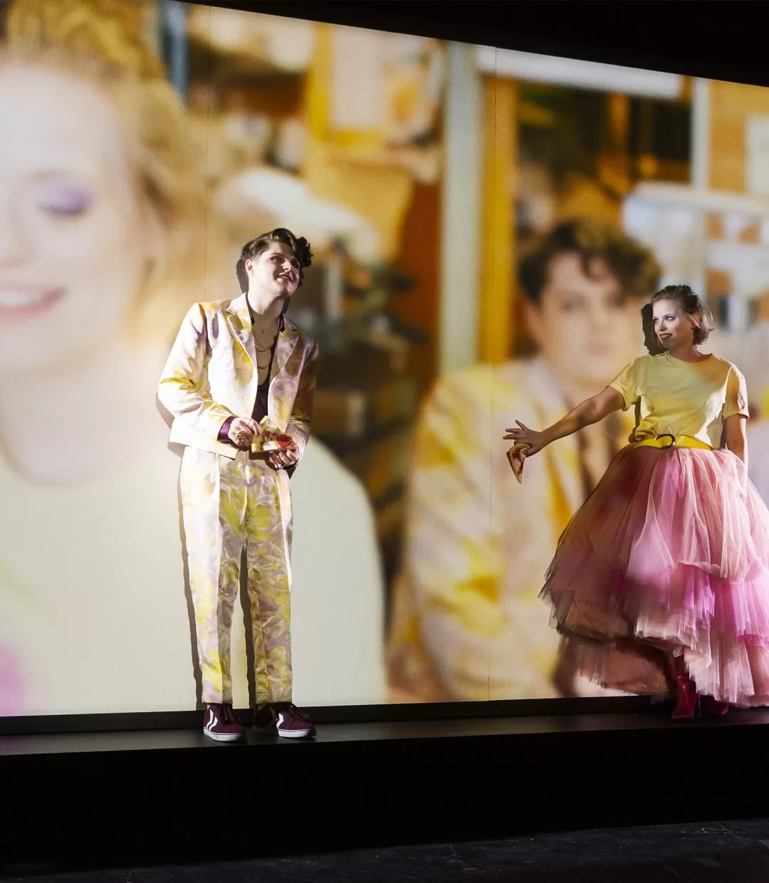 Zwei Schauspielende vor einer Videoleinwand schauen verträumt.