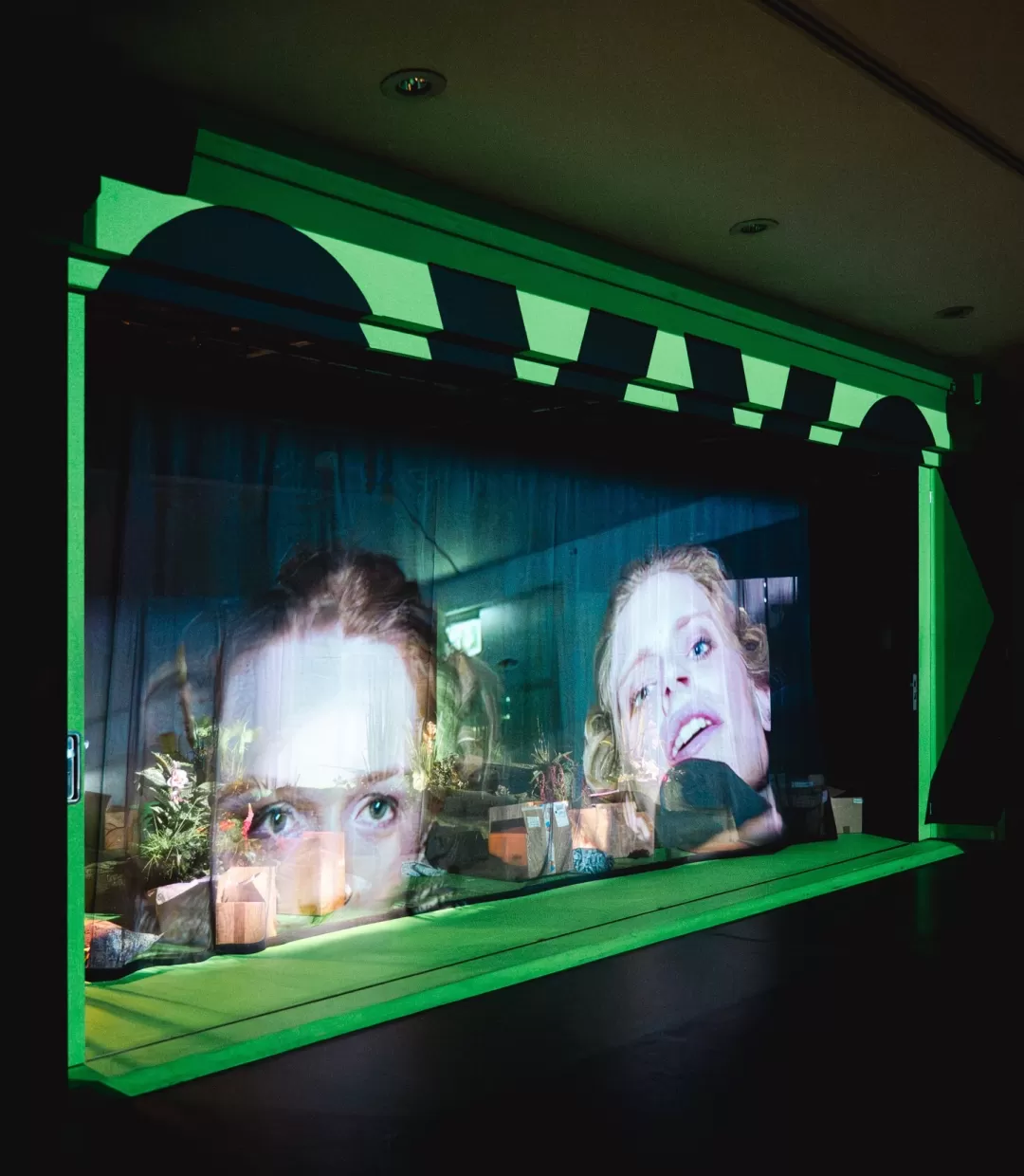 Leinwandprojektionen zweier Schauspielerinnen, singend.