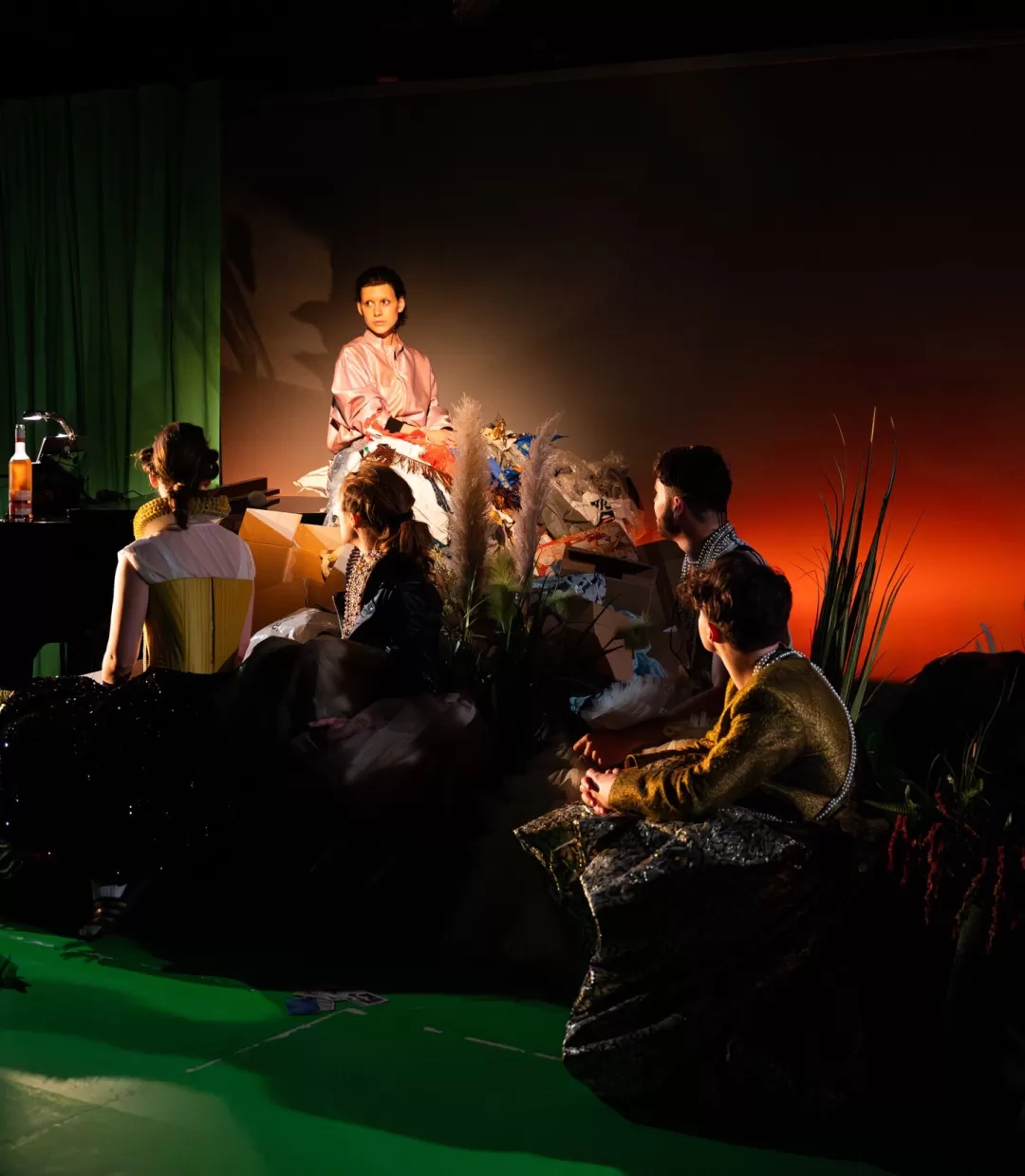 Eine Schauspielerin sitzt auf einem Klavierflügel, um sie herum andere Schauspieler*inne, die sie anschauen.