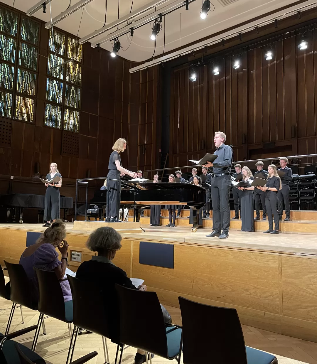 Studentin dirigiert Chor, zwei Solist*innen singen vorne an der Bühne