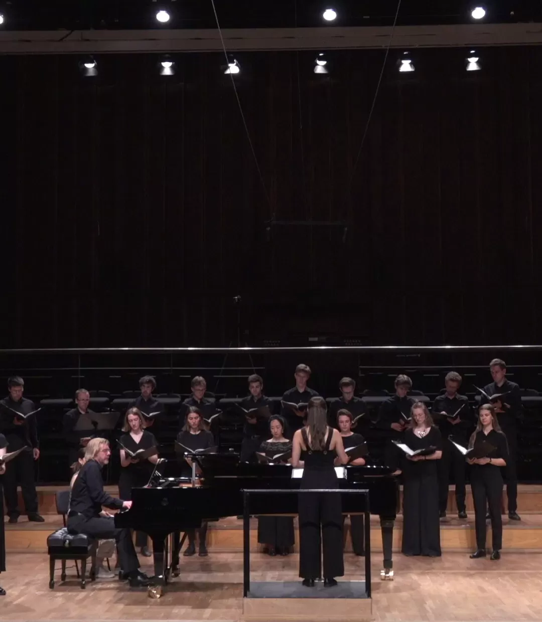 Frontalansicht: Solist und Solistin singen, im Hintergrund steht Chor