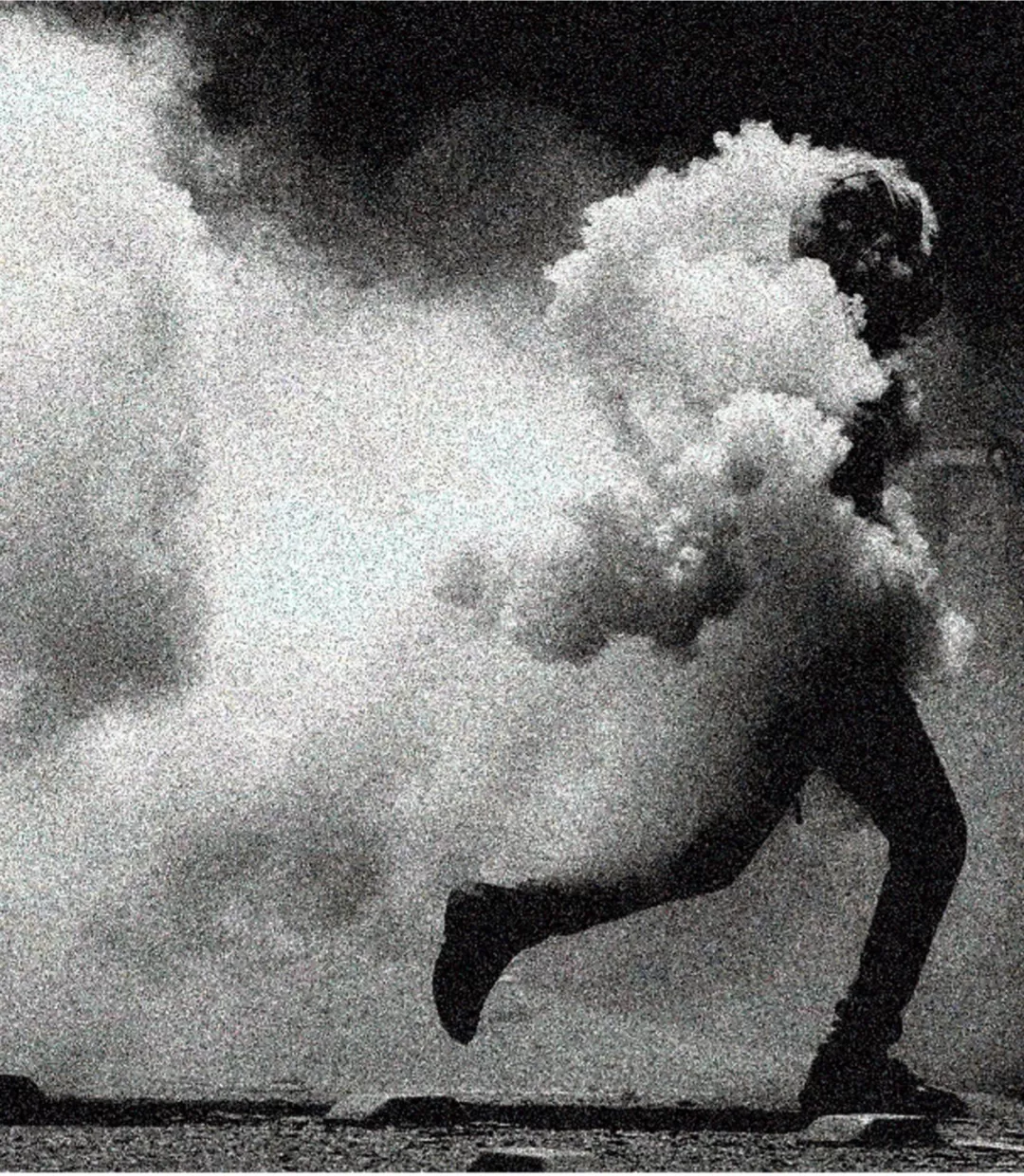 Ein schwarz-weiß Bild zeigt eine dunke Gestalt, die von links nach rechts durch das Bild rennt, umgeben von Rauchschwaden.