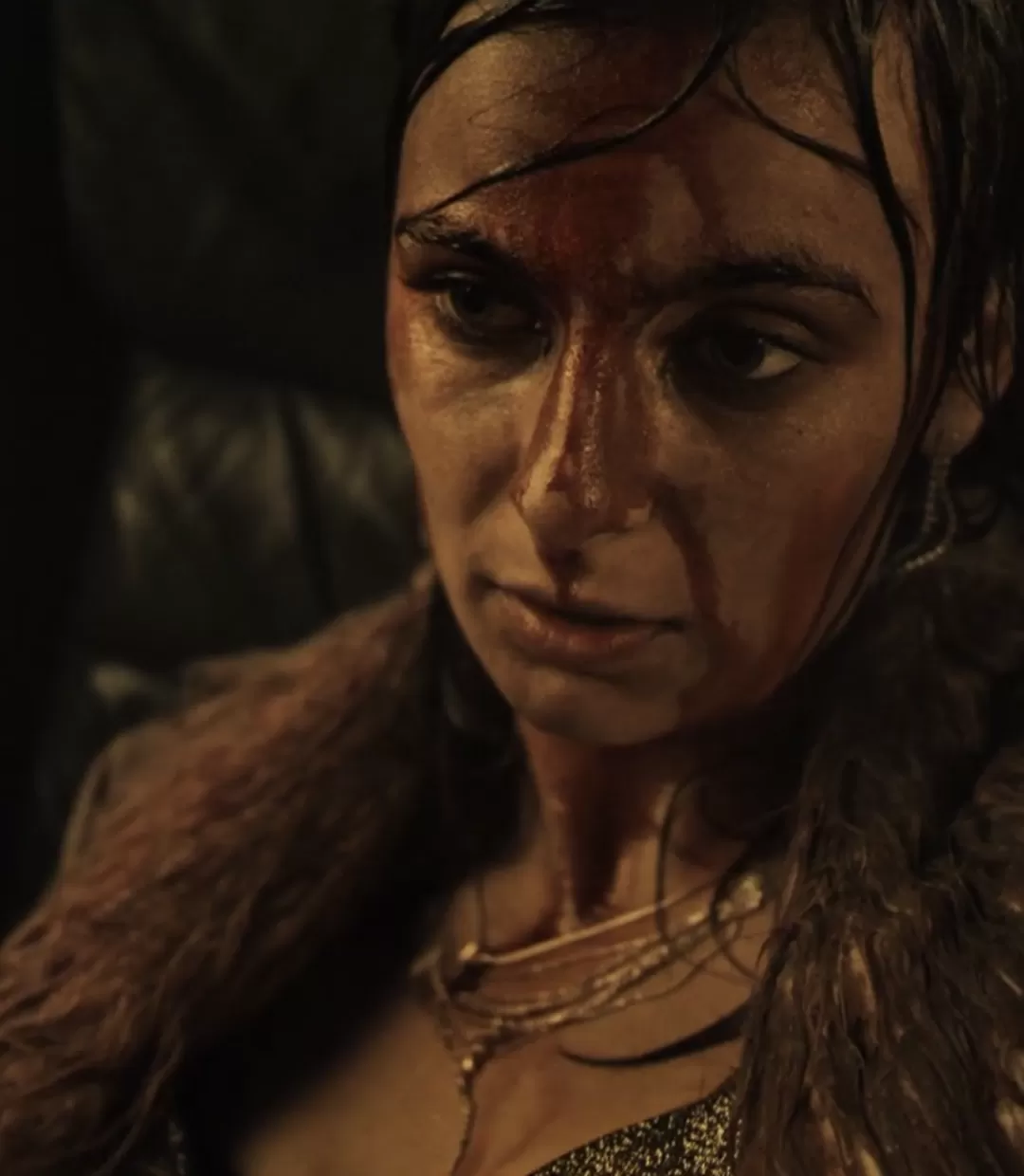 Frau sitzt in einem Auto mit nüchternem Blick und im Gesicht mit Blut bedeckt.