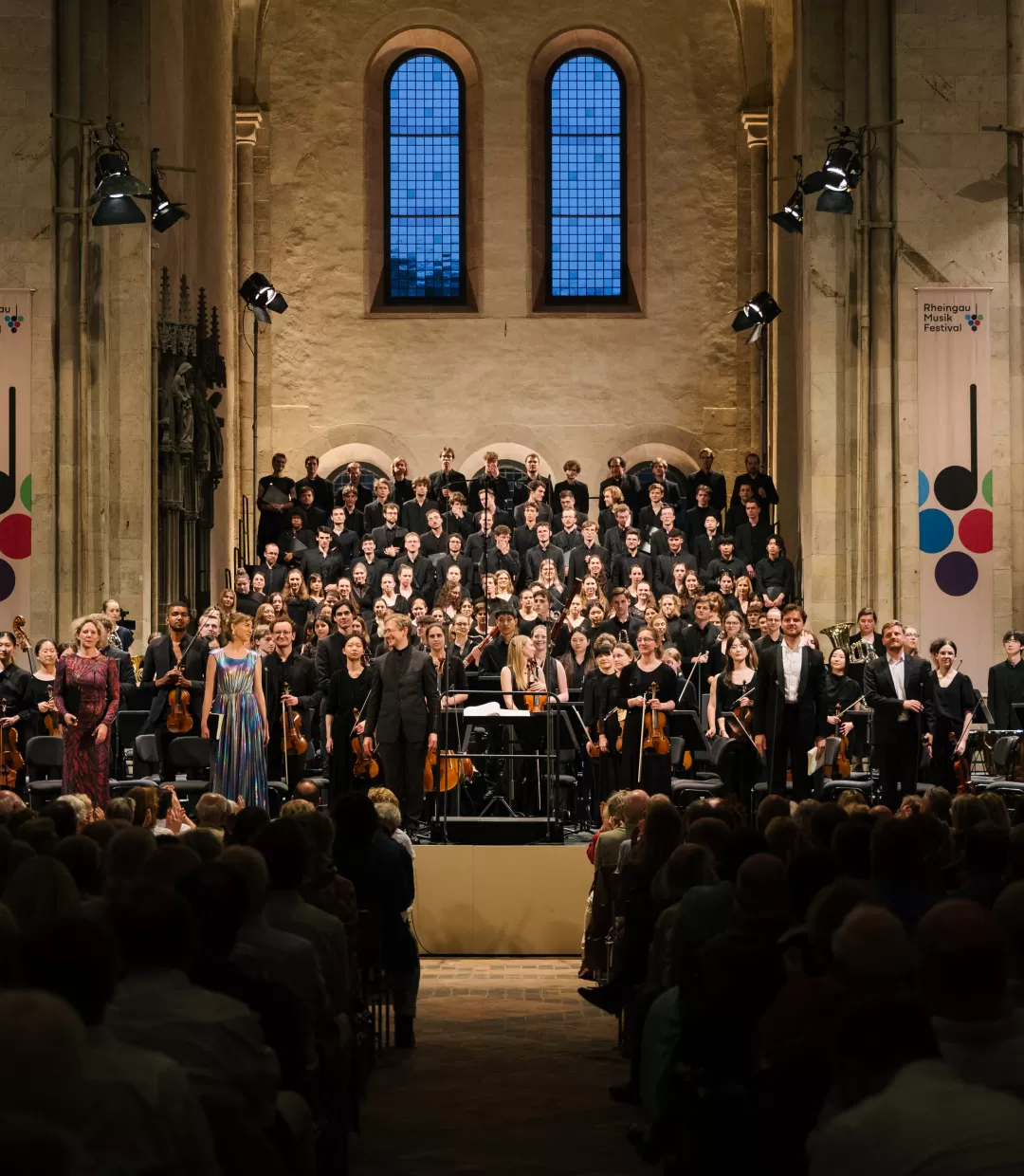 Schlussapplaus: Solist*innen und Florian Lohmann schauen ins Publikum, hinter ihnen Chor und Orchester