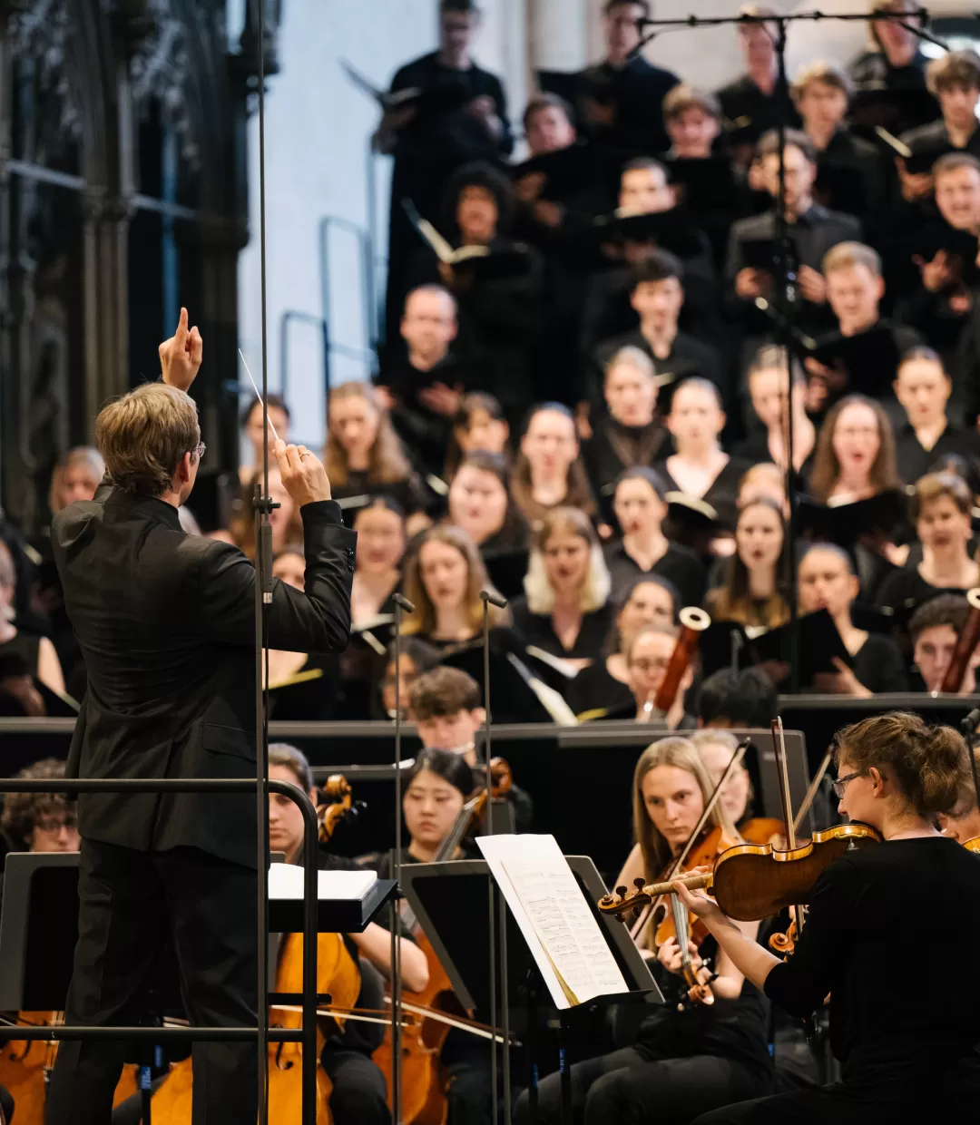 Florian Lohmann beim Dirigieren im Konzert von der Seite fotografiert, man sieht Teile des Orchesters und Chores