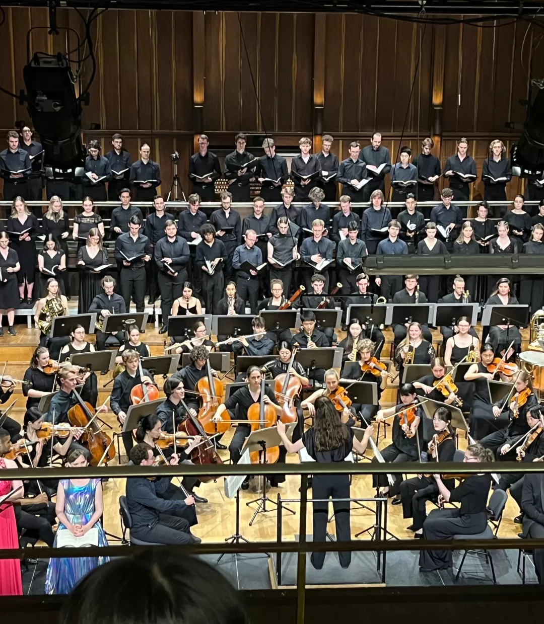 Blick auf Bühne im großen Saal, eine Studentin dirigiert Chor und Orchester