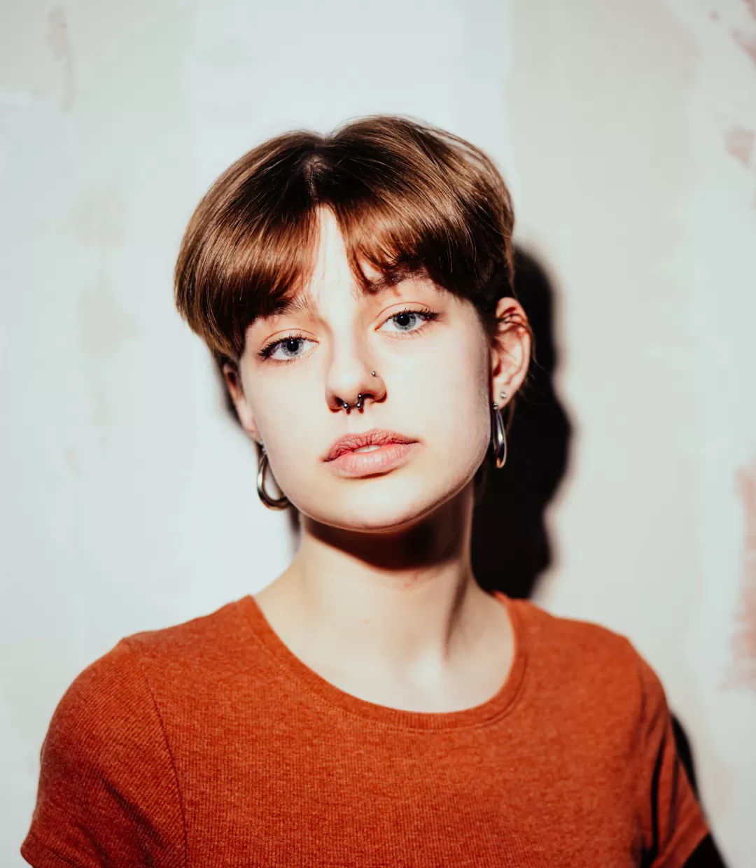 Portrait Paula Marie Schulze, orangefarbenes T-Shirt, im Hintergrund eine kahle, beige Wand