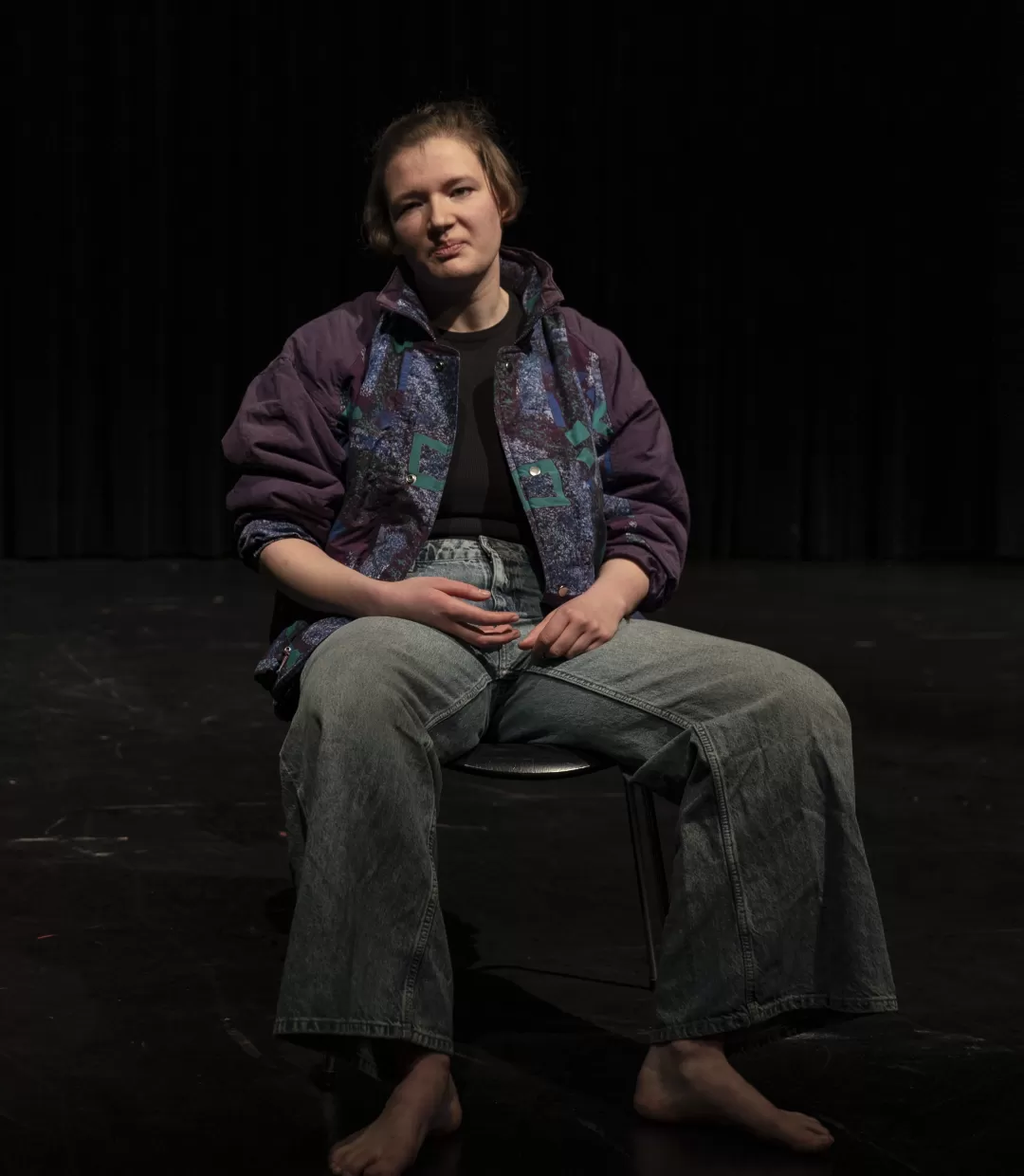 Frau in Jeans und Jacke sitzt breitbeinig und angepisst auf einem Stuhl