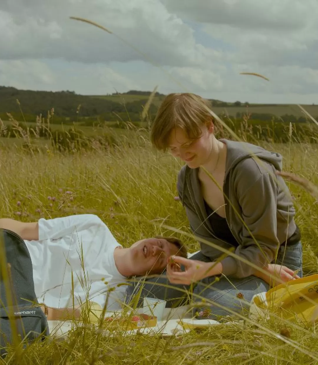 zwei Personen auf einer Wiese, eine liegend eine sitzend, nah beieinander