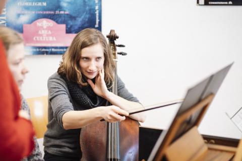 Eine junge Frau mit Cello zeigt mit dem Streicherbogen auf Noten. 
