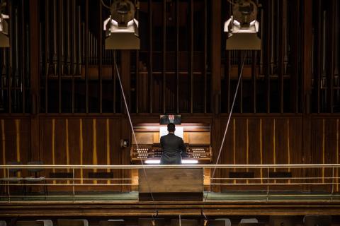 Rückansicht eines Organisten an der Orgel, aus der Ferne betrachtet.