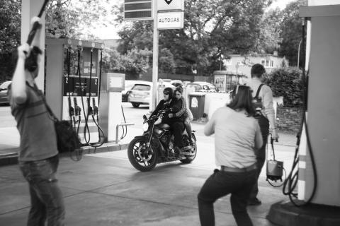 Zwei Personen fahren auf einem Motorrad in eine Tankstelle und werden dabei gefilmt.