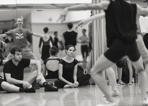 Im Tanzstudio, zwei Tanzstudierende sitzen auf dem Boden und sehen dem Training zu