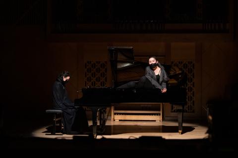 Ein Flügel, der mit einem Scheinwerfer von oben beleutet ist. Eine Person sitzt auf dem Klavierstuhl, die andere sitzt im geöffneten Flügel. Beide sind schwarz gekleidet.