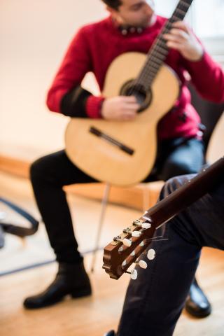 Unterricht im Fach Gitarre, im Vordergrund die Gitarre des Dozenten, im Hintergrund spielt der Student.