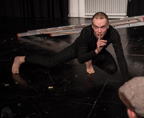 Max Böttcher wie ein Chamäleon auf dem Boden hockend, dem Publikum bedeutend leise zu sein. 