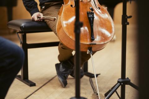 Cellist (man sieht nur die untere Hälfte seines Instruments und seine Hände), die Hand am Bogen angespannt.
