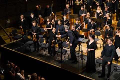 Der Dirigent schüttelt der Konzertmeisterin nach einem Konzert von Chor und Orchester auf der Bühne des Großen Saals die Hand.