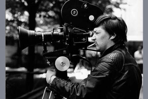 Rainer Werner Fassbinder an einer Filmkamera, Zigarette im Mund.
