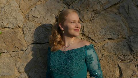 Johanna steht in einem Ballkleid vor einer Bruchsteinmauer und sieht in die Abendsonne.