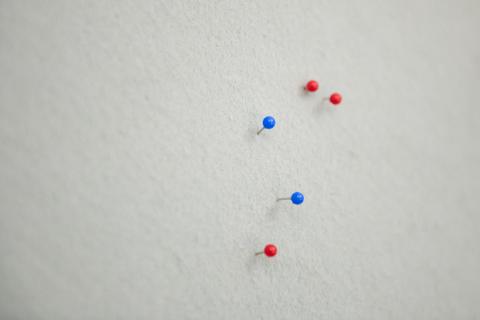 Stecknadeln mit blauen und roten Köpfen in einer weißen Pinnwand