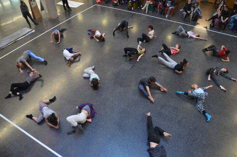 Eine große Gruppe Tänzer*innen auf dem Boden verteilt, von oben fotografiert.