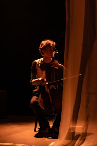 Cellist auf Theaterbühne, Blick nach rechts, transparenter Vorhang auf der rechten Seite 