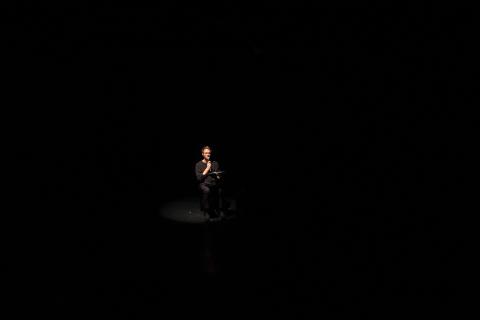 Ein Schauspieler sitzt in einem ansonsten dunklen Raum