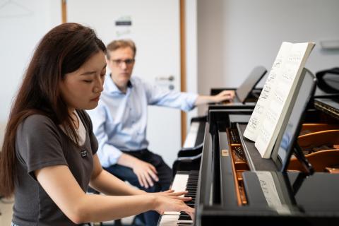 Klavier-Einzelunterricht: Im Vordergrund eine Studentin am Flügel, sie blickt konzentriert auf ihre Hände.