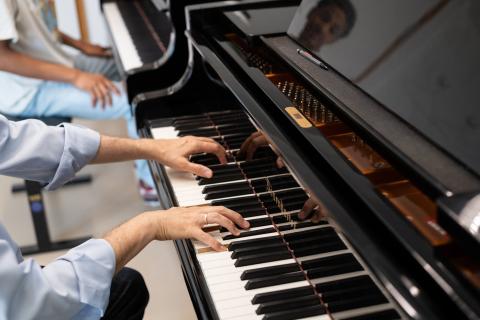 Klavier-Einzelunterricht: Nahaufnahme der Hände des Professors, der am Klavier dem Studenten etwas vorspielt.