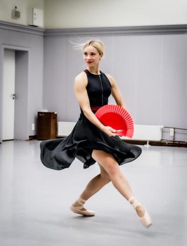 Eine Studentin tanzt im schwarzen Kleid und mit einem roten Fächer in der Hand.
