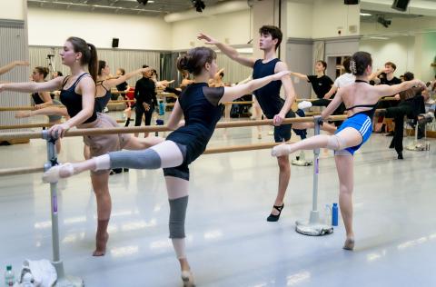 Vier Balletttänzer*innen an der Stange: Sie strecken das rechte Bein nach hinten (battement tendu) und den rechten Arm nach vorne