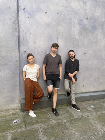 Die drei Musiker*innen des Sören Riesner Trios lehnen an einer grauen Betonwand.