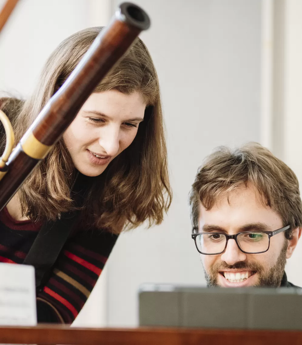Eine junge Frau mit Fagott und ein junger Mann am Cembalo, beide lächeln.