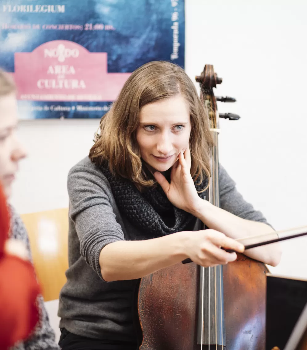 Eine junge Frau mit Cello zeigt mit dem Streicherbogen auf Noten.